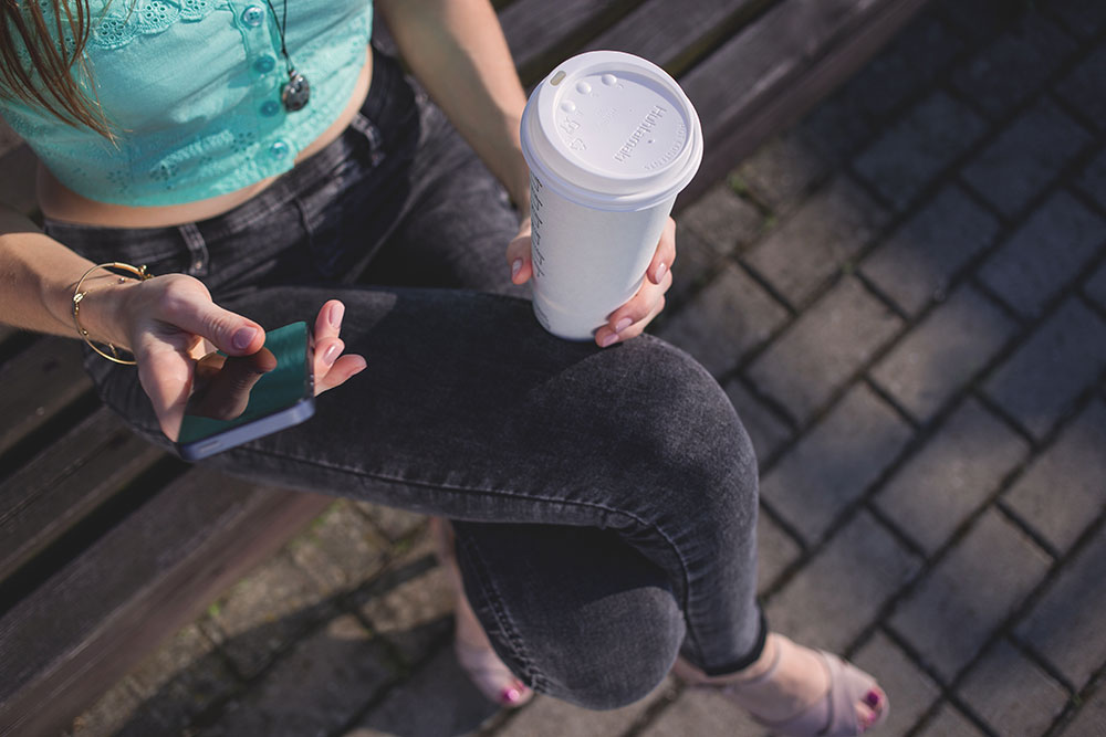 woman with coffee doing search on mobile phone