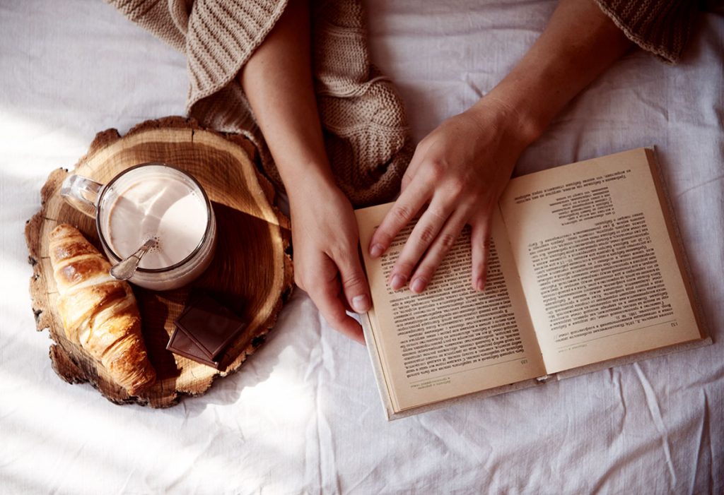 woman with cocoa, croissant, and a book