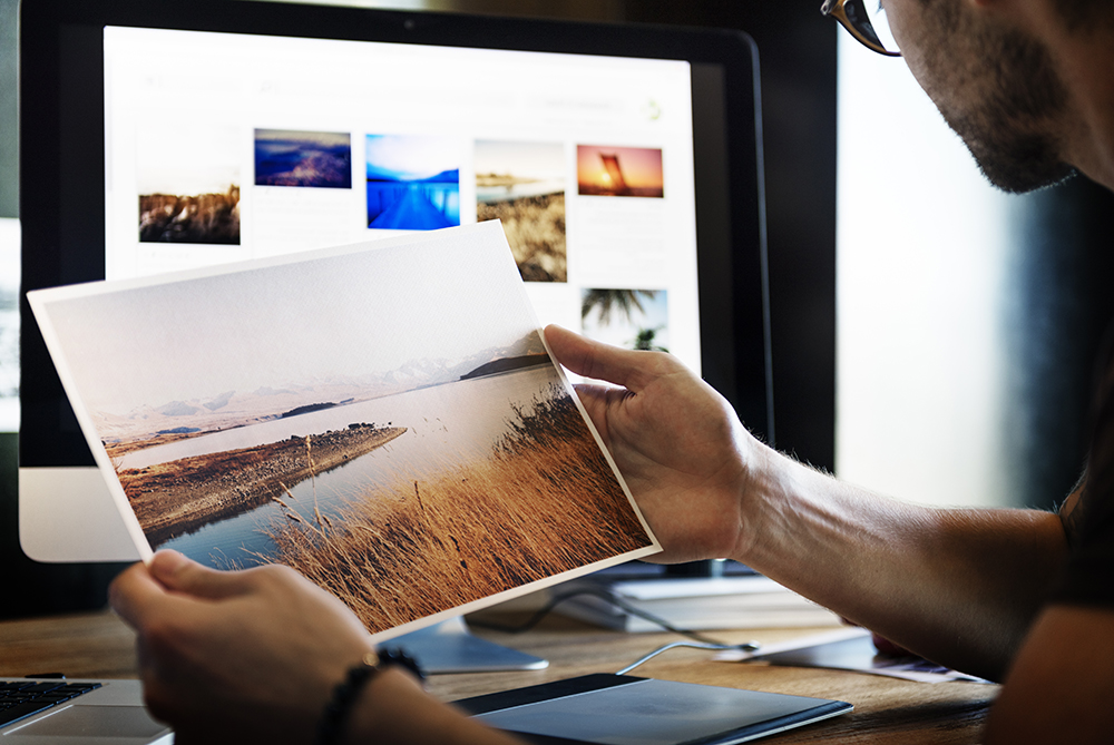 someone holding photos and looking at computer