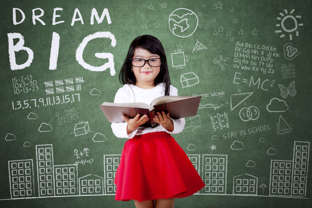 girl with book in front of blackboard with dream big and science designs